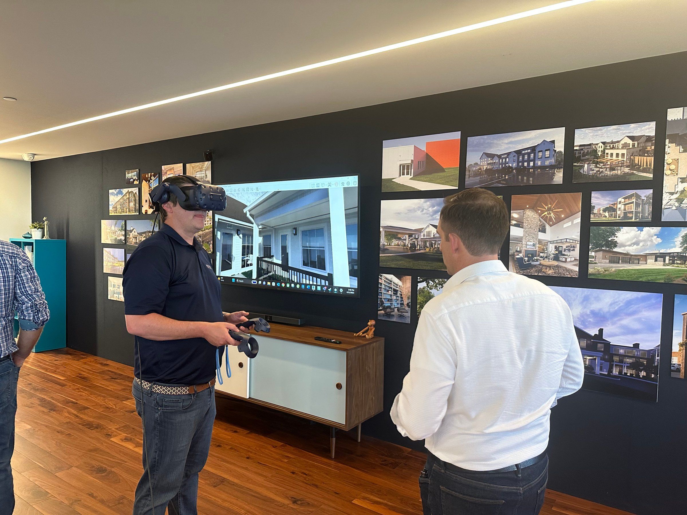 A client team member in a VR headset walks through a design while a colleague looks at project renderings on the wall
